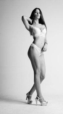 Beyaz iç çamaşırlı ve yüksek topuklu bir kız beyaz arka planda poz veriyor.. 