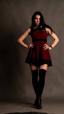 Karanlık stüdyoda şık giyinmiş esmer bir kadın poz veriyor.  