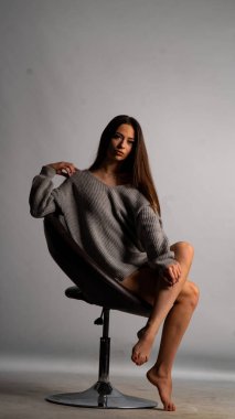 Güzel seksi kız, kısa gri bir elbise, beyaz bir arka plan sandalyesi