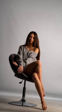 Güzel seksi kız, kısa gri bir elbise, beyaz bir arka plan sandalyesi