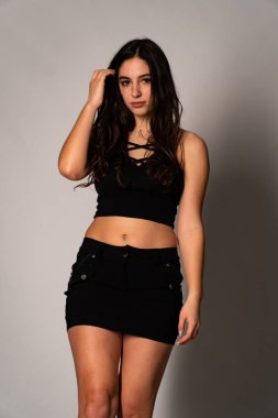 Siyah elbiseli, siyah saçlı, açık renk stüdyo arka planında poz veren güzel bir kadın. 