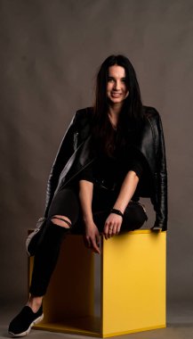 Karanlık stüdyoda şık giyinmiş esmer bir kadın poz veriyor.  