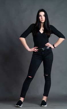 Yüksek tahta koltukta bacak bacak üstüne atmış esmer bir kadının portresi. Geniş paçalı pantolon giyen şık bir kız. Gri arkaplanda stüdyo çekimi