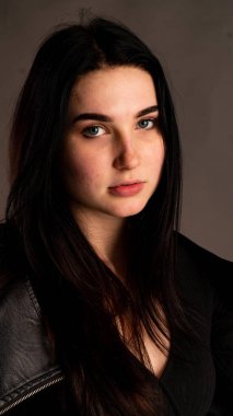 Karanlık stüdyoda şık giyinmiş esmer bir kadın poz veriyor.  