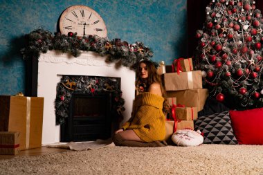 Noel süslemeli stüdyoda şöminenin yanında poz veren güzel esmer genç bir kadın. 
