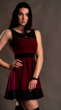 Karanlık stüdyoda şık giyinmiş esmer bir kadın poz veriyor.  