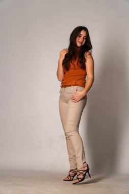 Güzel esmer manken şık kıyafetler içinde, aydınlık odada poz veriyor. 