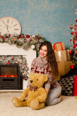 Koyu renk elbiseli güzel bir kadın Noel süslemeli stüdyoda şöminenin yanında poz veriyor. 