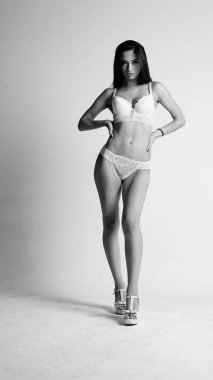 Beyaz iç çamaşırlı ve yüksek topuklu bir kız beyaz arka planda poz veriyor.. 