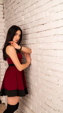 Koyu renk saçlı, kırmızı elbiseli, karanlık stüdyoda poz veren genç ve seksi bir kadın..