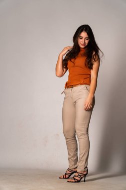 Güzel esmer manken şık kıyafetler içinde, aydınlık odada poz veriyor. 