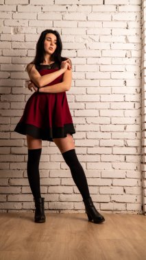 Koyu renk saçlı, kırmızı elbiseli, karanlık stüdyoda poz veren genç ve seksi bir kadın..