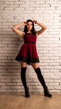 Koyu renk saçlı, kırmızı elbiseli, karanlık stüdyoda poz veren genç ve seksi bir kadın..