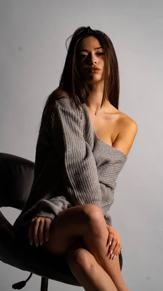 Hermosa chica sexy, con un vestido gris corto, una silla de fondo blanca. —  Fotos de Stock