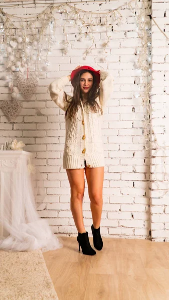 Kırmızı şapkalı ve kalın kazaklı güzel seksi kadın tuğla duvarda poz veriyor. 