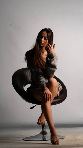 Krásná sexy dívka, pózování krátké šedé šaty, bílé pozadí židle — Stock fotografie