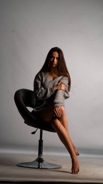 Güzel seksi kız, kısa gri bir elbise, beyaz bir arka plan sandalyesi