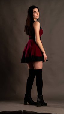 Karanlık stüdyoda şık giyinmiş esmer bir kadın poz veriyor.  