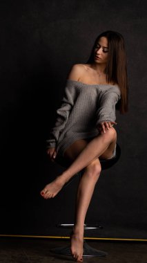 Stüdyoda siyah bir arka planda duran kolları olan güzel gri elbiseli seksi bir genç. 