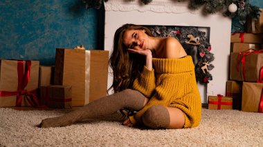 Noel süslemeli stüdyoda şöminenin yanında poz veren güzel esmer genç bir kadın. 