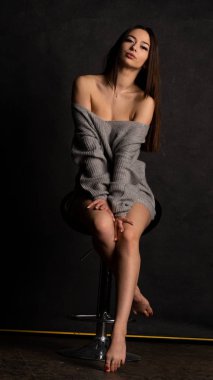 Stüdyoda siyah bir arka planda duran kolları olan güzel gri elbiseli seksi bir genç. 