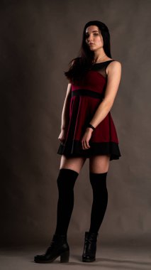 Karanlık stüdyoda şık giyinmiş esmer bir kadın poz veriyor.  