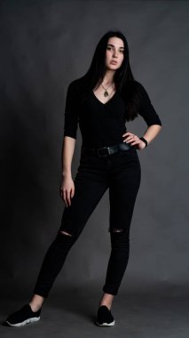 Yüksek tahta koltukta bacak bacak üstüne atmış esmer bir kadının portresi. Geniş paçalı pantolon giyen şık bir kız. Gri arkaplanda stüdyo çekimi