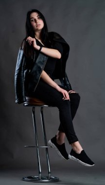 Karanlık stüdyoda şık giyinmiş esmer bir kadın poz veriyor.  