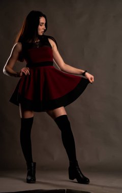 Karanlık stüdyoda şık giyinmiş esmer bir kadın poz veriyor.  