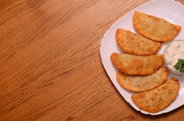 Özbek Doğu Tatar mutfağı, et ve suluguni ile cheburek peynirli sebze ve Yeşiller ahşap bir masa üzerinde beyaz bir tabak içinde.