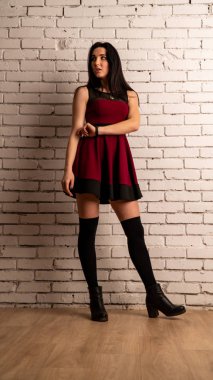 Koyu renk saçlı, kırmızı elbiseli, karanlık stüdyoda poz veren genç ve seksi bir kadın..