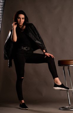 Karanlık stüdyoda şık giyinmiş esmer bir kadın poz veriyor.  