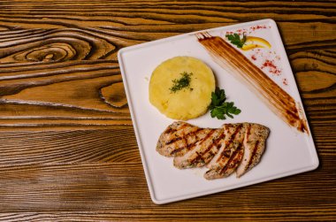 Yakın plan iki parça çiğ ızgara et kırmızı biber ve sosla süslenmiş patates cipsi ve sebze salatasıyla servis edilmiş ahşap tabakta..