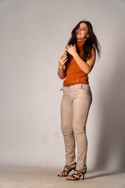 Güzel esmer manken şık kıyafetler içinde, aydınlık odada poz veriyor. 