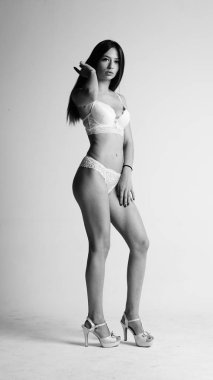 Beyaz iç çamaşırlı ve yüksek topuklu bir kız beyaz arka planda poz veriyor.. 