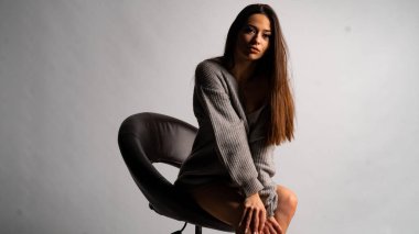 Güzel seksi kız, kısa gri bir elbise, beyaz bir arka plan sandalyesi