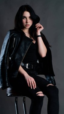 Karanlık stüdyoda şık giyinmiş esmer bir kadın poz veriyor.  