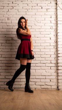 Koyu renk saçlı, kırmızı elbiseli, karanlık stüdyoda poz veren genç ve seksi bir kadın..