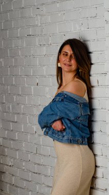 esmer kız yeşil bir ceket ve beyaz tuğla duvarın yanında sutyen standları