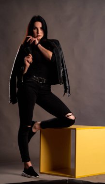 Karanlık stüdyoda şık giyinmiş esmer bir kadın poz veriyor.  