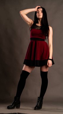 Karanlık stüdyoda şık giyinmiş esmer bir kadın poz veriyor.  