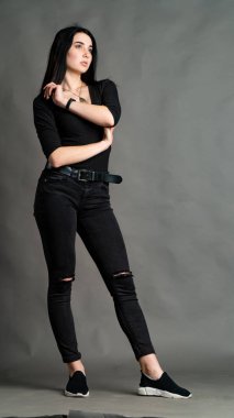 Yüksek tahta koltukta bacak bacak üstüne atmış esmer bir kadının portresi. Geniş paçalı pantolon giyen şık bir kız. Gri arkaplanda stüdyo çekimi