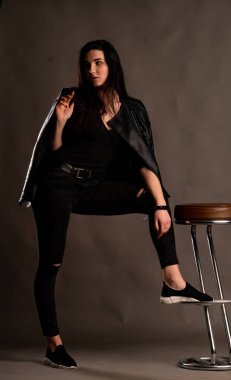 Karanlık stüdyoda şık giyinmiş esmer bir kadın poz veriyor.  