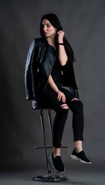 Karanlık stüdyoda şık giyinmiş esmer bir kadın poz veriyor.  