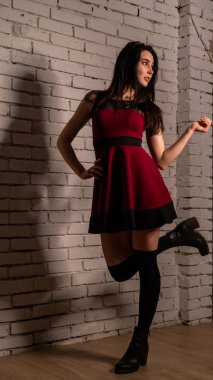 Koyu renk saçlı, kırmızı elbiseli, karanlık stüdyoda poz veren genç ve seksi bir kadın..