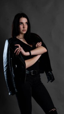 Karanlık stüdyoda şık giyinmiş esmer bir kadın poz veriyor.  