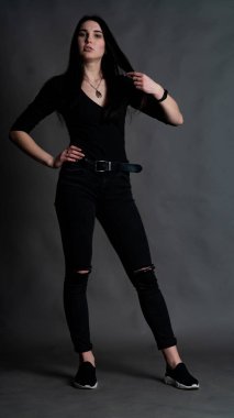 Yüksek tahta koltukta bacak bacak üstüne atmış esmer bir kadının portresi. Geniş paçalı pantolon giyen şık bir kız. Gri arkaplanda stüdyo çekimi