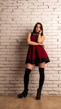 Koyu renk saçlı, kırmızı elbiseli, karanlık stüdyoda poz veren genç ve seksi bir kadın..