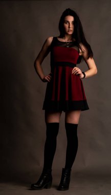 Karanlık stüdyoda şık giyinmiş esmer bir kadın poz veriyor.  