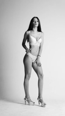 Beyaz iç çamaşırlı ve yüksek topuklu bir kız beyaz arka planda poz veriyor.. 